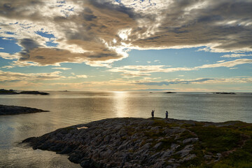 Young couple controlling the drone with remote control at the Norwegian coastline at sunset