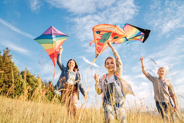 Smiling gils and brother boy running with flying colorful kites on the high grass meadow in the...