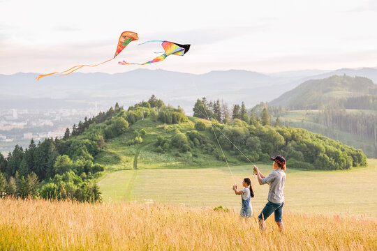 Kids playing: sister with a brother with launching colorful kites - popular outdoor toy on the high grass hills meadow. Happy childhood moments or outdoor time spending concept image.