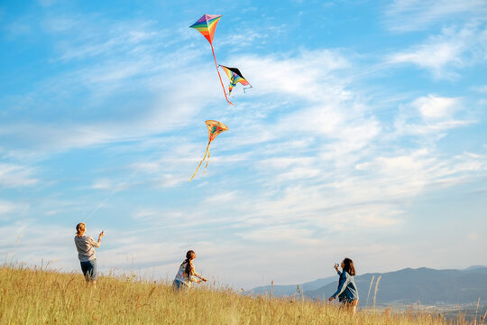 Children kite fighting with flying colorful kites - popular outdoor toy on the high grass mountain meadow. Happy childhood moments or outdoor time spending concept image.