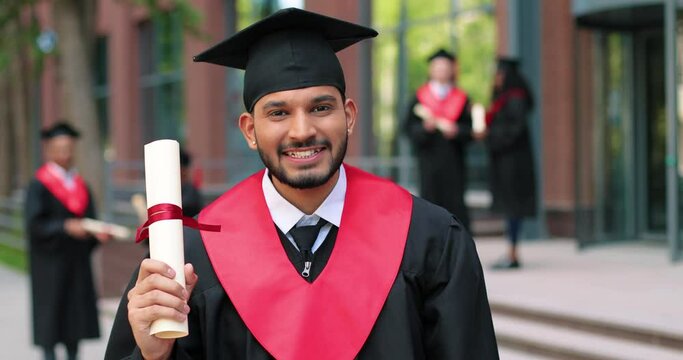 Young graduated boy holding his graduation degree convocation ceremony. Attractive multiracial student graduate posing towards the camera during the ceremony
