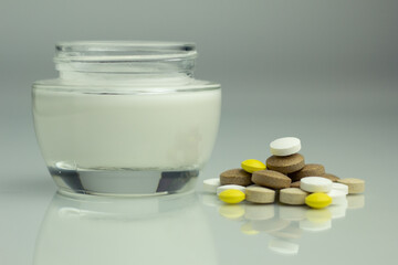Closeup of supplements for clear skin (vitamin C, zinc, ashwagandha, vitamin B) and a jar of moisturising cream.