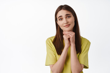 Fototapeta premium Portrait of young silly girl making adorable face, lean on hands and asking for smth, begging, contemplating beautiful thing, standing over white background