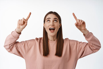 Image of excited smiling girl student pointing, looking up amused, checking out promo deal, staring...