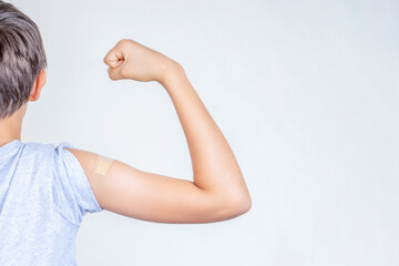 Teenage boy with bandage plaster on his arm makes fist and flexes her bicep after vaccination....