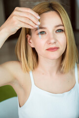 Fototapeta premium A beautiful young woman holds a glass-dropper with cosmetical serum upon her face. Skin treatment and cosmetology concept.