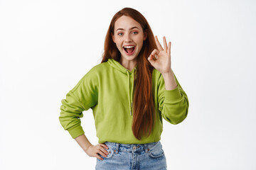 Obraz na płótnie Canvas Zero problems. Smiling cute ginger girl show okay OK sign, good job, praise something nice, approve great thing, recommending, white background