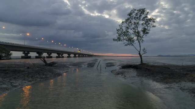 Timelapse day to night over reflection of mangrove tree beside build structure Penang Second Bridge
