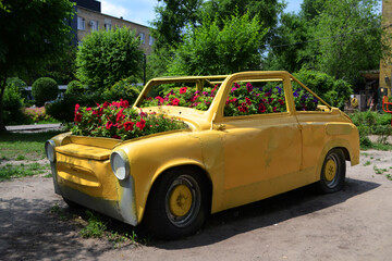 Retro car of yellow color with flowers, a flower bed from the car in the park.
