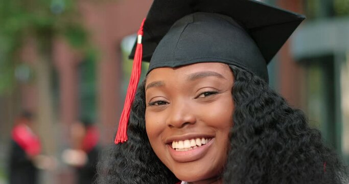 Young graduated curly girl holding her graduation degree convocation ceremony. Attractive multiracial student graduate posing towards the camera during the ceremony