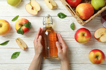 Female hands hold apple vinegar on white wooden background