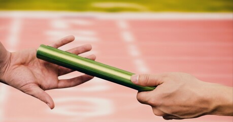 Mid section of hand passing a baton against sports field in background - obrazy, fototapety, plakaty