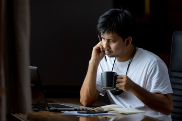 Young asian male using computer sitting at home office desk, new normal, living during the coronavirus crisis or covid19 outbreak	