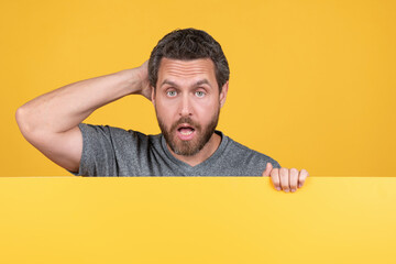 shocked mature man with surprised face behind yellow paper for copy space, surprise