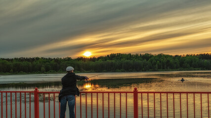 Obraz premium A fisherman catches fish from a bridge at sunset.