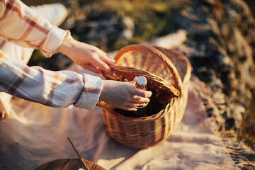 A woman's hand pulls out of a picnic basket a bottle of red wine.