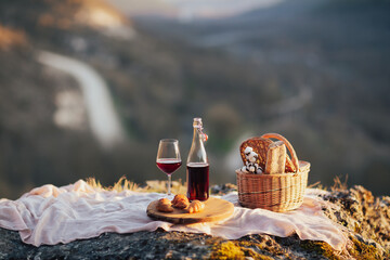 Summer picnic outdoors with basket with baguette, wooden plate of croissants and bottle and glass...