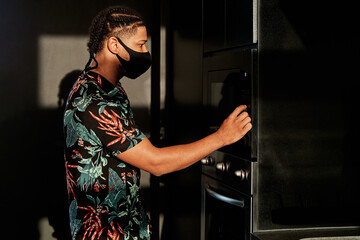 Fototapeta na wymiar young latin man using oven with mask in the middle of quarantine