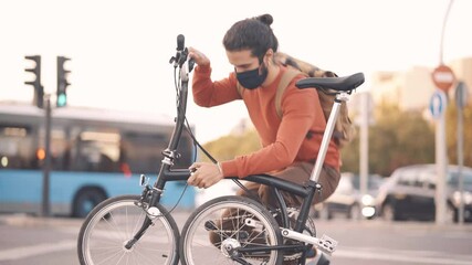 Stock video of man wearing face mask folding his bike in the street. - Powered by Adobe