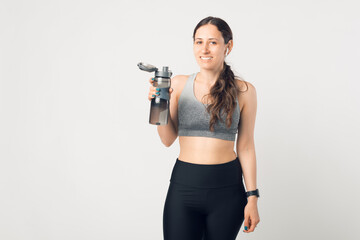 Portrait of sport woman in sportswear standing over white background and holding water bottle