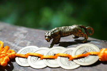A metal tiger figurine and a bunch of Chinese coins on a tree branch.