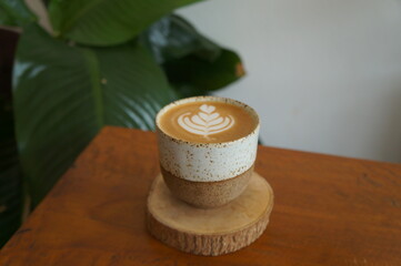 Hot coffee cappuccino in a ceramic mug placed on a wooden table.