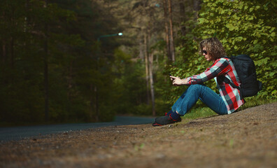 Male tourist sitting near the road with mobile phone.