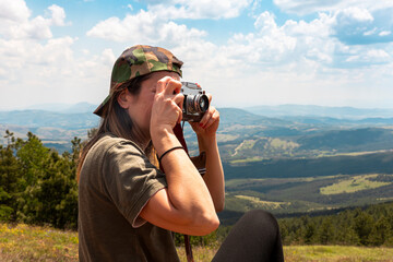 Tourist girl photographing with vintage photo camera at the top of the mountain peak