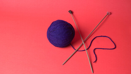 A Piece of knitting with color threads ball of yarn and a knitting needle on red background.