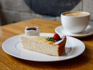 Piece of cheese casserole or cheesecake, garnished with raspberry jam and cup cappuccino coffee on wooden table. Breakfast in cafe, top view, horizontal Traditional russian ukrainian breakfast