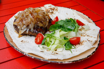 Fried calf's liver with shallots and vegetable salad on pita bread on red wooden table, close up, horizontal.