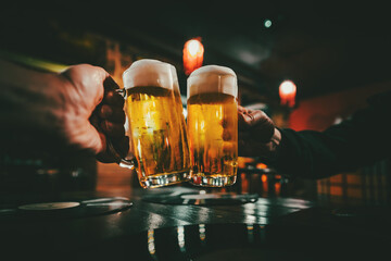 Closeup view of a two glass of beer in hand. Beer glasses clinking in bar or pub - obrazy, fototapety, plakaty