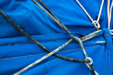 Tied ropes in a knot in the middle on a blue sailcloth, close-up. A nautical knot made of ropes on...
