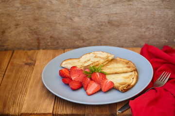 Pancakes, thin pancakes with fresh strawberries. On a wooden background. Copy space.