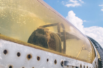 Close-up of a military fighter pilot's cockpit. A crack is visible on the glass, which has turned yellow with age. Decommissioned military equipment. Airplane pilot seat