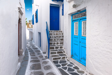 Traditional greek house with blue door and staircase in narrow city alley. Mykonos Island, Greece.