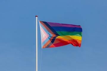 Worldwide LGBTQ community concept with progress pride flag (new design of rainbow flag) waving in the air with blue sky, Celebration of gay pride, The symbol of lesbian, gay, bisexual and transgender. - obrazy, fototapety, plakaty