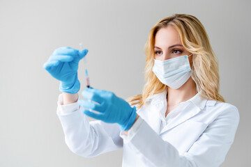 Confident and beautiful female medical professional with long blond hair preparing syringe for covid-19 vaccination. He holds syringe in his hands.