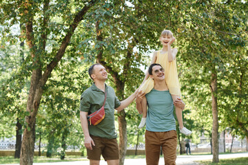 Fototapeta premium Happy gay couple walking together with adopted daughter in the park