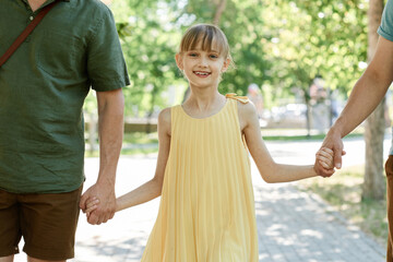Portrait of little girl smiling at camera while walking in the park together with her family