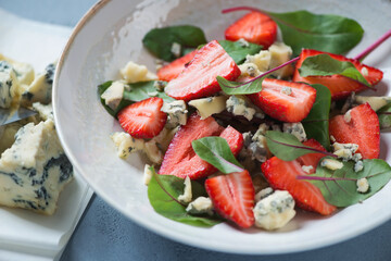 Closeup of salad with fresh strawberry, mangold leaves and blue cheese served in a beige plate, selective focus