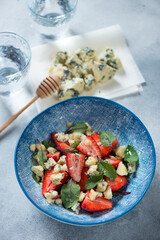 Blue bowl with mangold, strawberry and gorgonzola cheese salad, vertical shot on a light-blue stone background