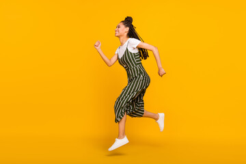 Fototapeta na wymiar Full length photo of impressed hurrying dark skin lady wear striped clothes jumping high running fast isolated yellow color background