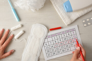 Woman marking critical menstrual days on calendar with hygiene products