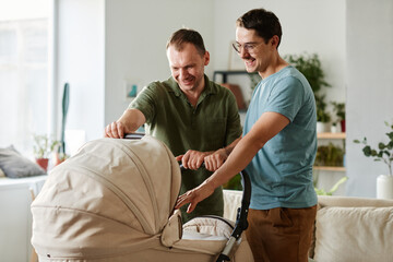 Happy young gay couple standing in the room with baby stroller they adopting the baby