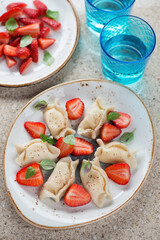 Cottage cheese dumplings served with fresh strawberries, vertical shot on a beige marble background, selective focus