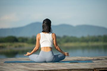 Fototapeta na wymiar Woman on a yoga mat to relax in the park at mountain lake. Calm woman with closed eyes practicing yoga, sitting in Padmasana pose on mat, Lotus exercise, attractive sporty girl in sportswear.