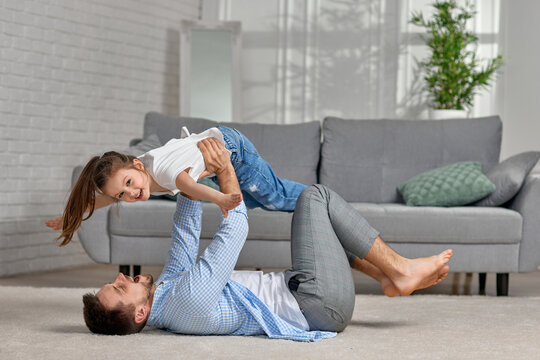 father lying on carpet floor and lifting little child girl