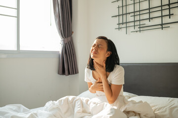 Morning sickness. Young pregnant woman sitting on bed, covering her mouth feeling nauseous during...