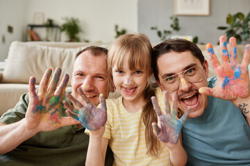 Portrait of happy gay family with child showing their painted hands and smiling at camera